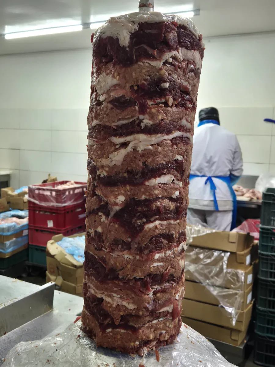 Rulou crud de vită și berbec, cu straturi de carne și grăsime așezate cu mâna pe tijă.