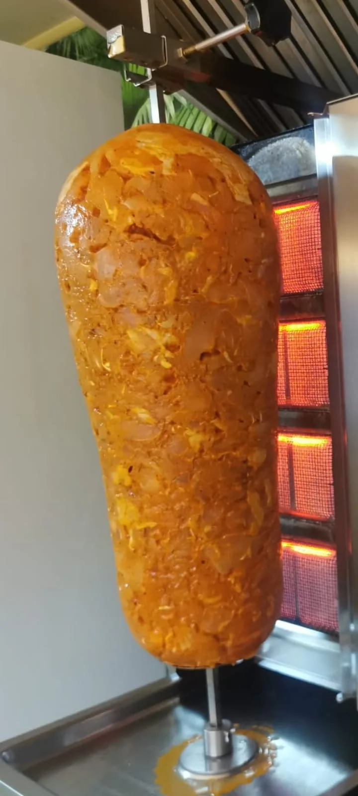 Rulou de pui condimentat pe rotisor vertical, cu arzătoarele aprinse în spate.